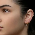 Studioaufnahme einer Frau mit einem Curated Ear aus mehreren Ohrläppchen-Piercings und einem Helix-Ring
