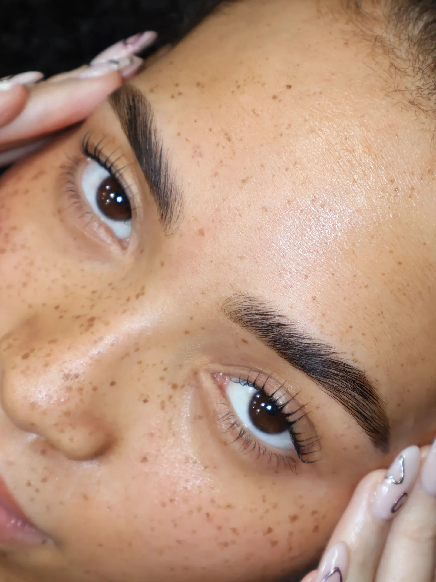Nahaufnahme natürlich gelifteter Wimpern nach einem koreanischen Wimpernlift, weiche, klar getrennte Rundung mit luftiger Struktur auf sommersprossiger Haut