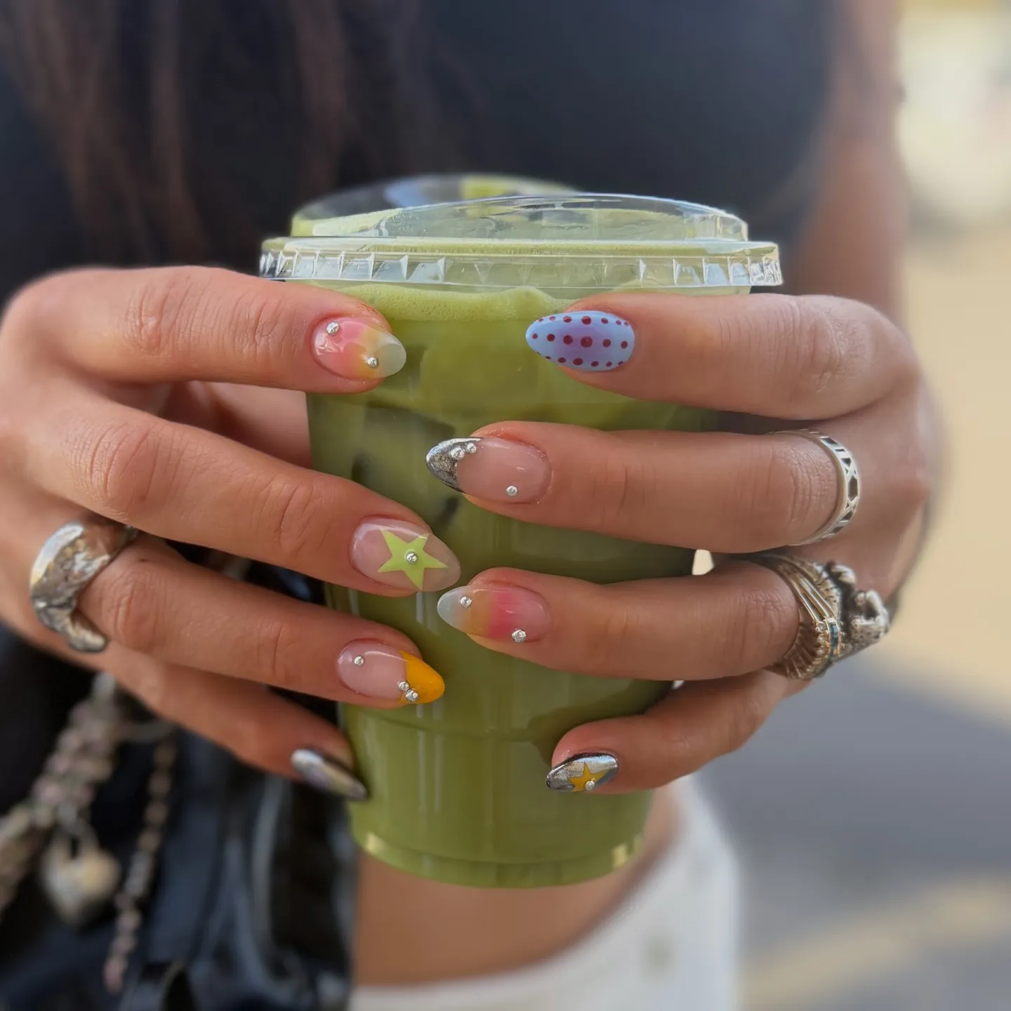 Gemischtes Nailart-Set mit kleinen Kristall-Piercings, Sternmotiven und bunten Akzenten auf mandelförmigen Nägeln