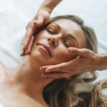 Frau entspannt während einer sanften Lymphdrainage im Gesicht, während die Hände der Fachkraft leicht über ihre Wangen gleiten